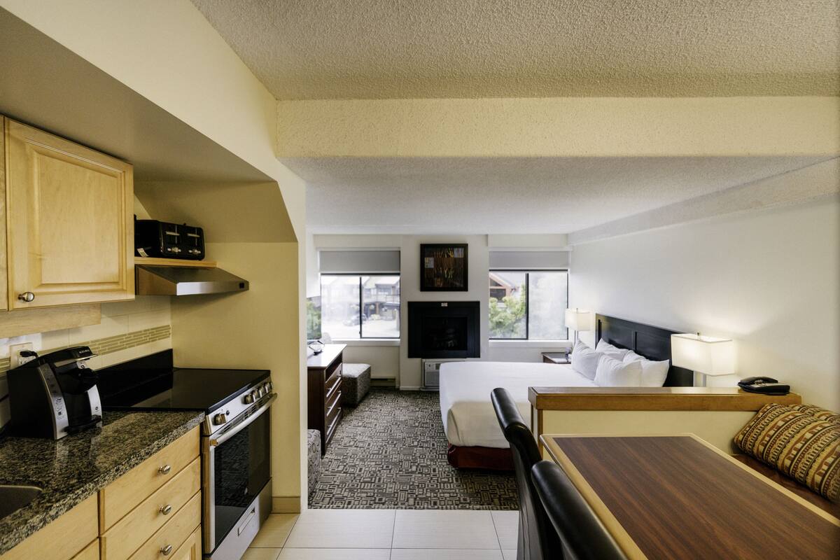 Habitación de hotel compacta con kitchenette, una cama con cabecera, una mesita de noche y una ventana con vistas.