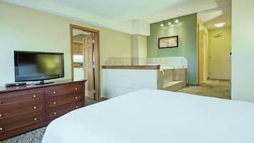 Habitación de hotel con cama, televisor en una cómoda, baño con ducha y puerta que da a otra habitación.