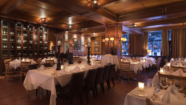 A restaurant with multiple tables set for dining, wooden paneling on the walls, and a view of snow outside the windows. - Mountain Side Hotel Whistler by Executive (Whistler)