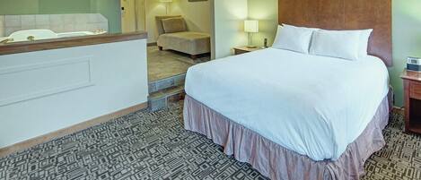 Una habitación de hotel con una cama grande, un escritorio, una silla y una mesita de noche con lámpara.