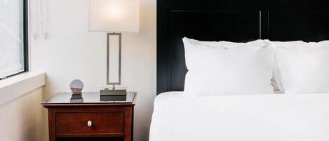 Una habitación de hotel con cama, mesita de noche, lámpara y ventana.