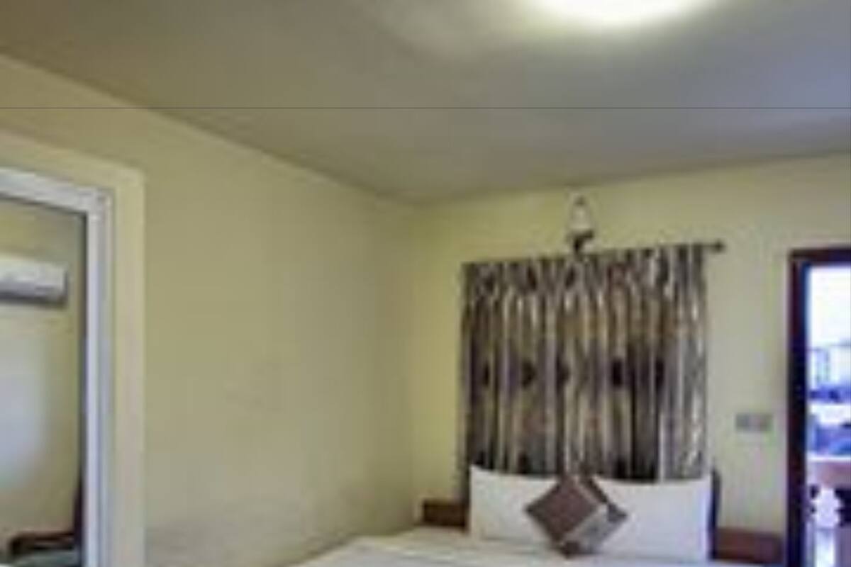 A hotel room with a bed, a bedside table, a mirror, and a window with curtains.