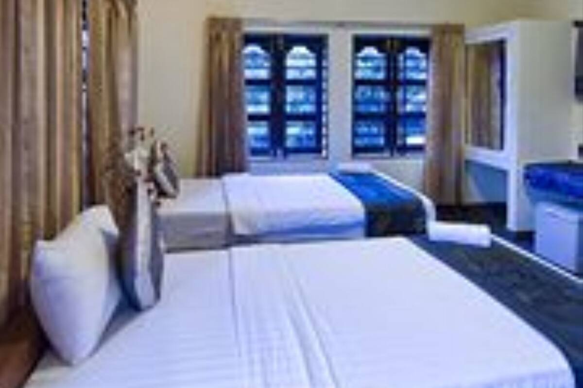 A hotel room with two beds, a desk, and a window with curtains.
