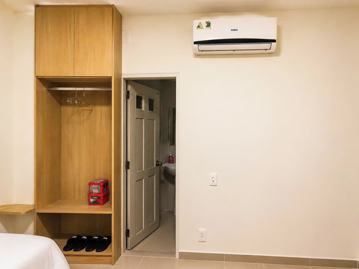 Una habitación con armario, cama, un caja roja de almacenamiento y un equipo de aire acondicionado.