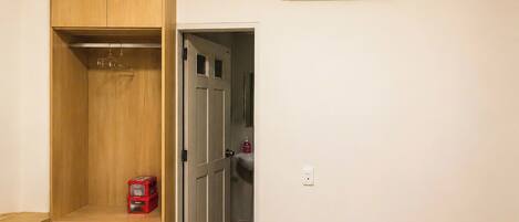 Una habitación con armario, cama, un caja roja de almacenamiento y un equipo de aire acondicionado.