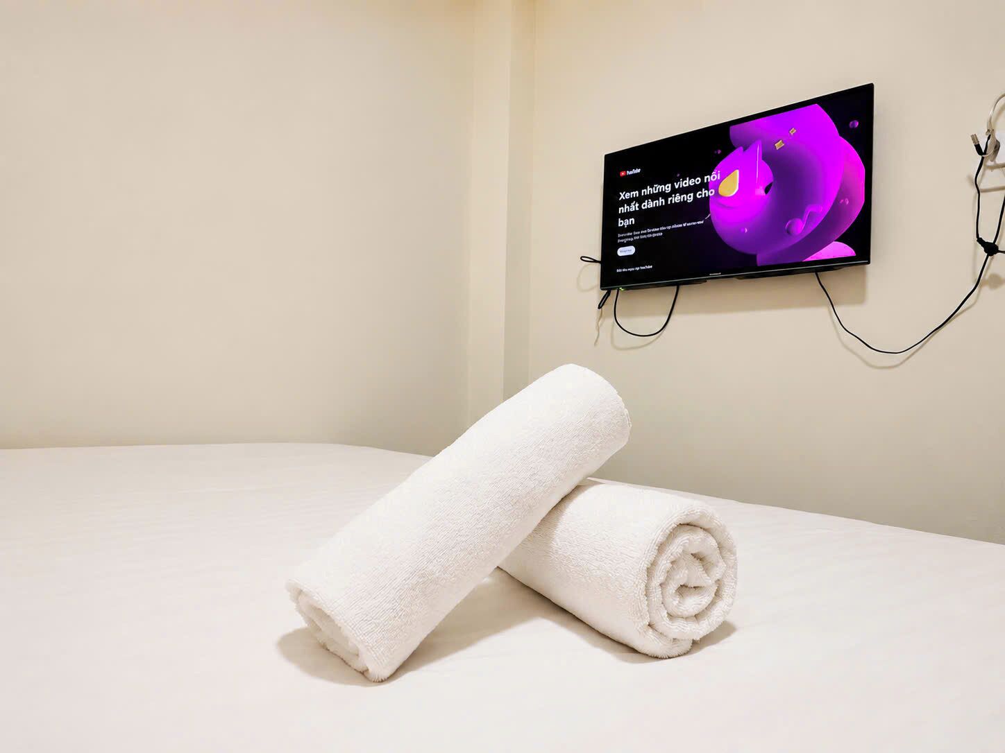A bed with a white towel and a television mounted on the wall displaying a video.