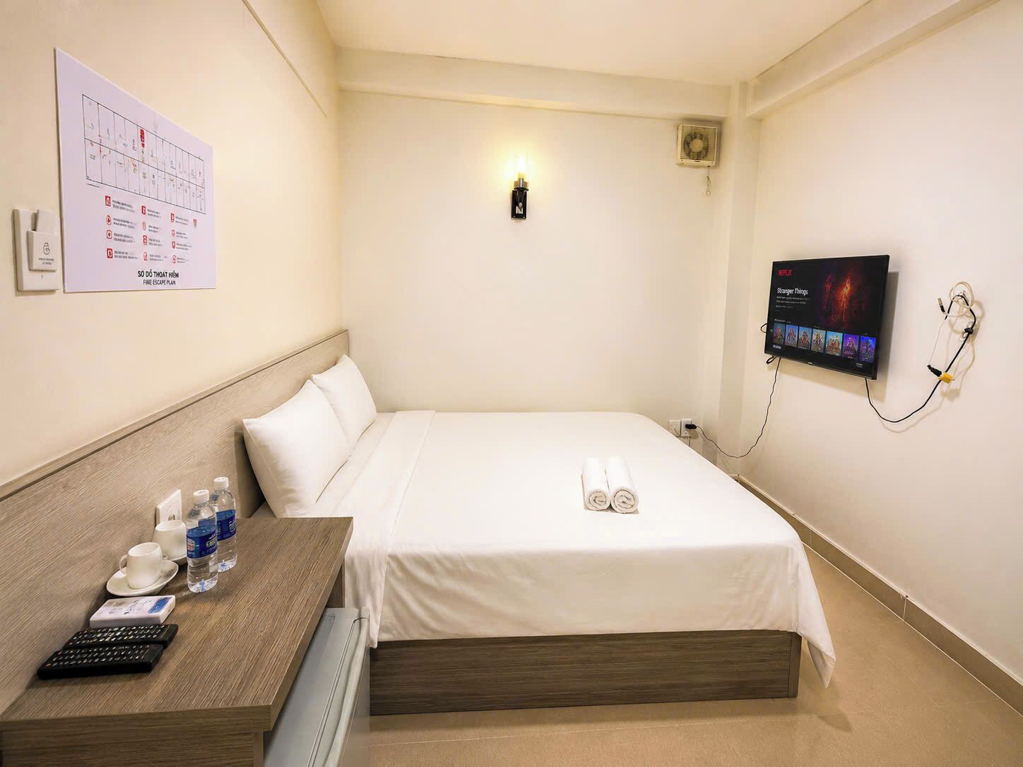Habitación de hotel con cama, escritorio con teclado, televisor y plano de evacuación en la pared.