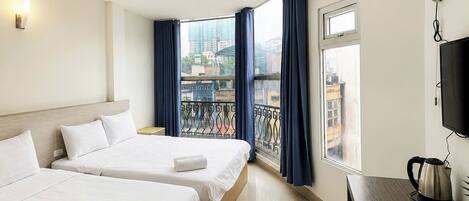 Habitación de hotel con dos camas, un escritorio con hervidor, televisión y balcón con cortinas.