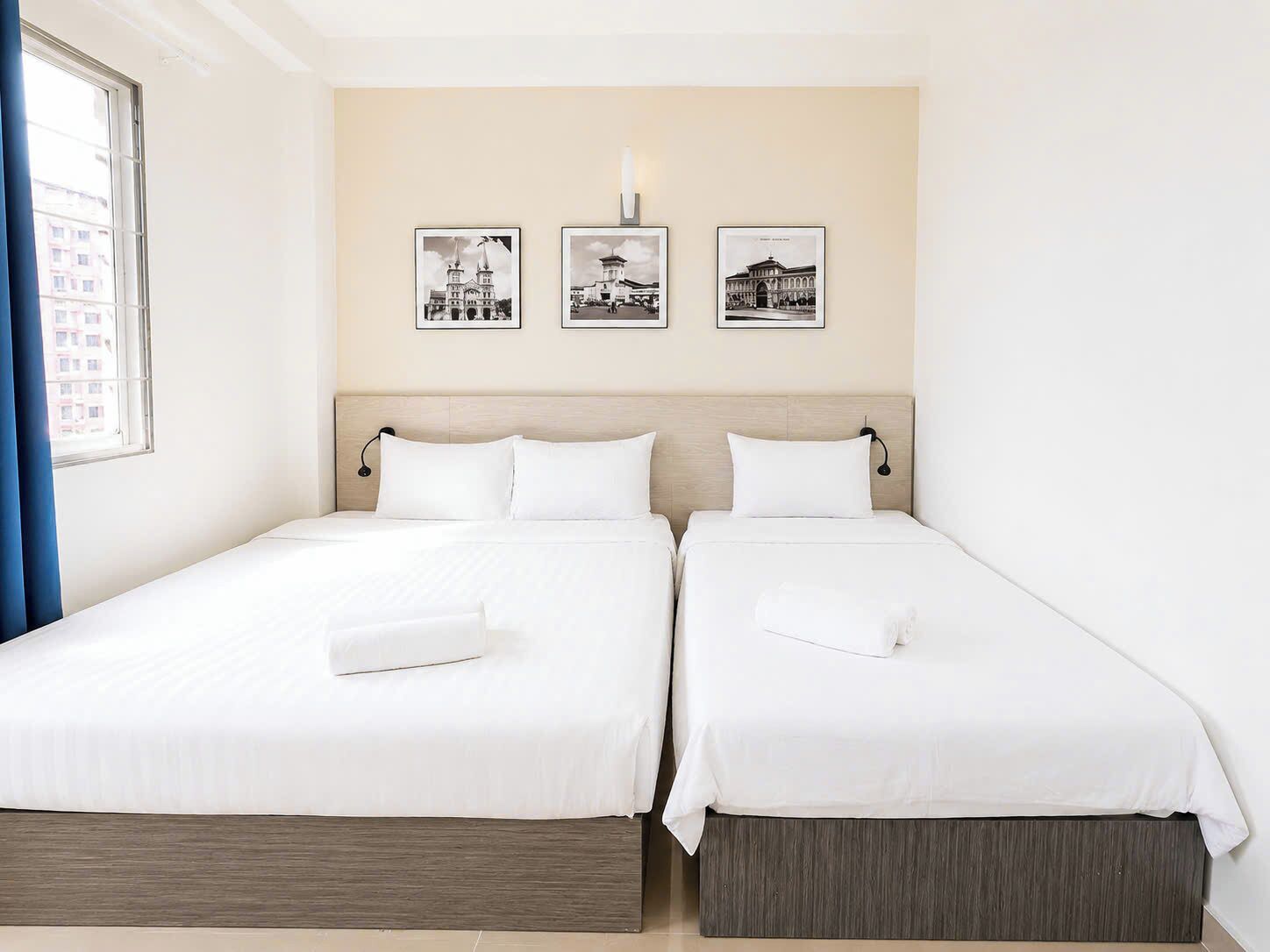 A hotel room with two beds, a headboard, and three black-and-white photographs on the wall.
