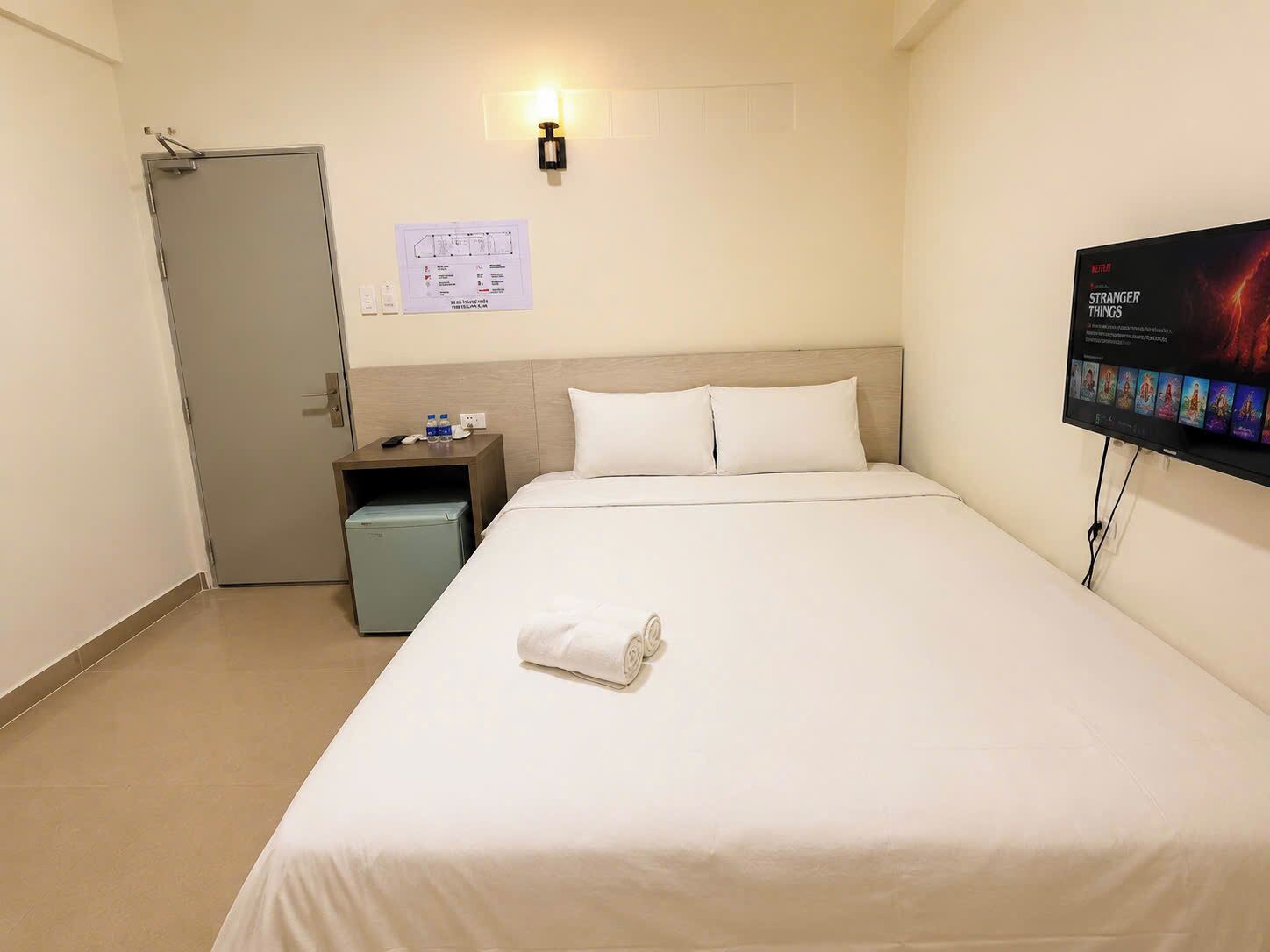A hotel room with a bed, a nightstand, a wall-mounted TV, and a door.