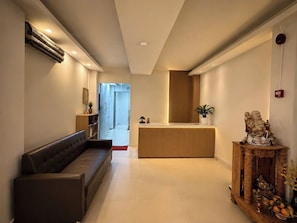 A modern hotel lobby with a reception desk, a seating area, and a decorative statue. - Hikari Stay - Bui Vien CBD (Ho Chi Minh City)