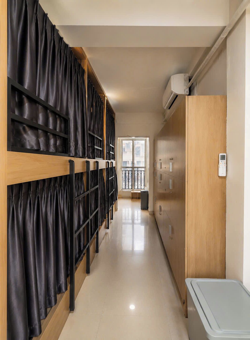 A hallway with a row of black curtains, a wooden wardrobe, and a white trash bin.