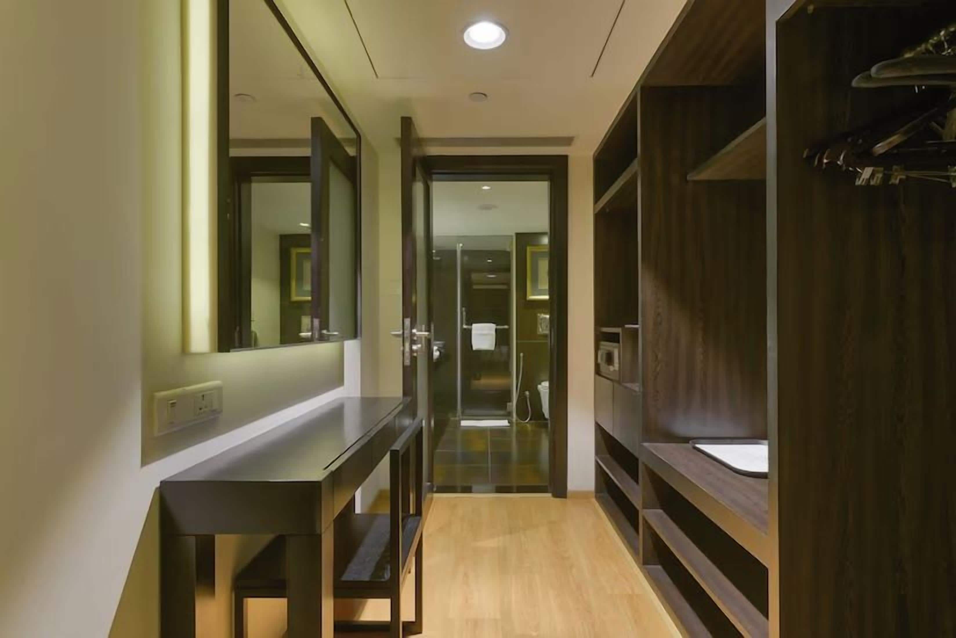 A hallway with a mirror, a wooden bench, and a door leading to a bathroom.