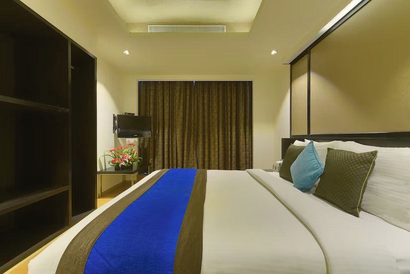 Habitación de hotel con una cama grande, un televisor de pantalla plana, un escritorio con lámpara y una cortina.