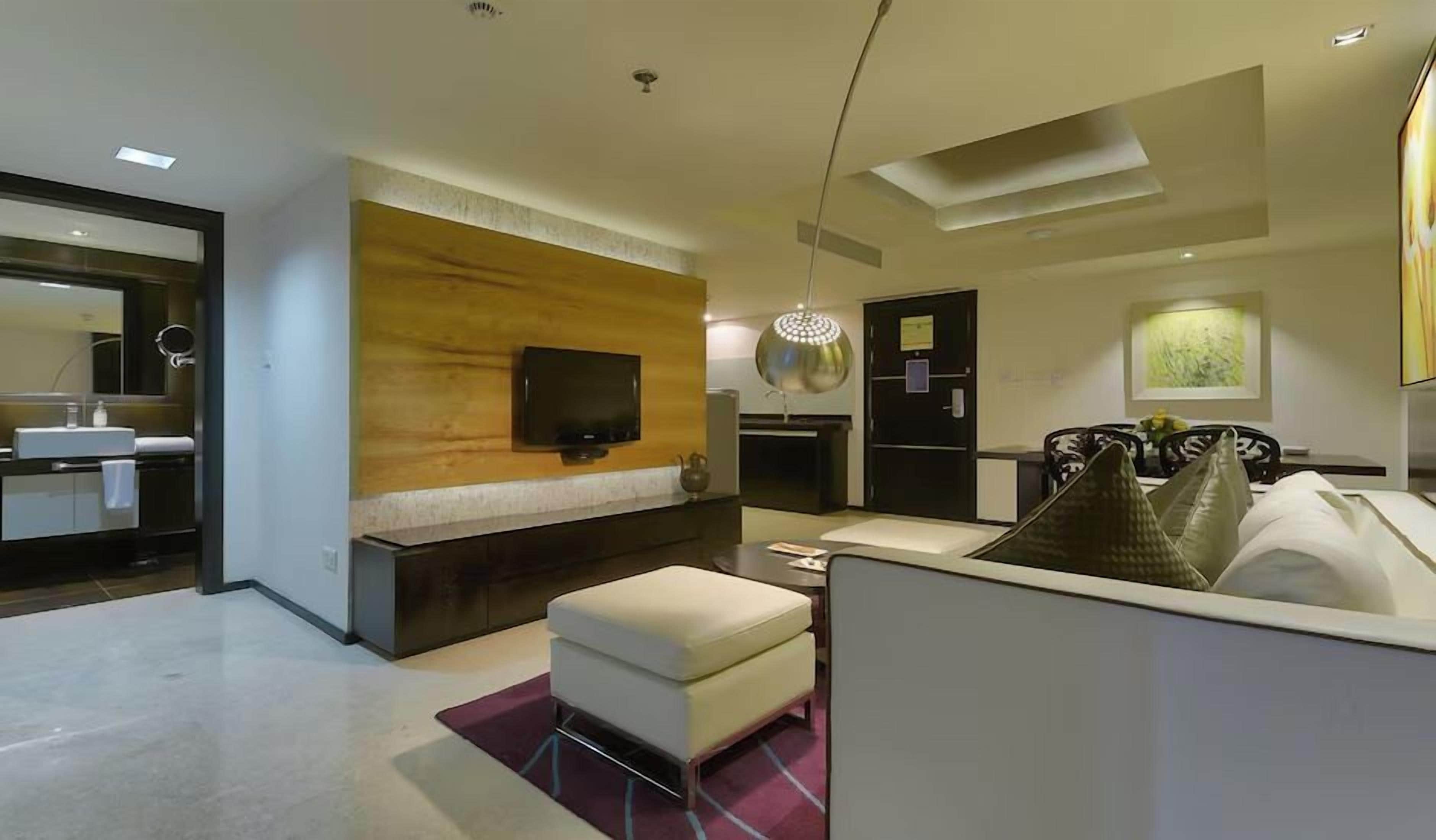 A modern living room with a flat-screen TV, a wooden accent wall, a sofa, and a dining area with a chandelier.
