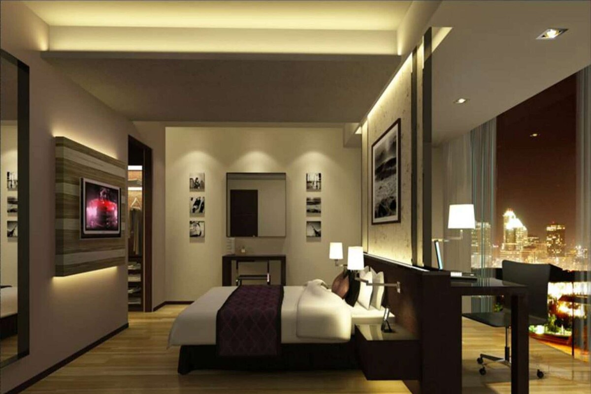 Un hotel moderno con una cama grande, un escritorio con una silla, un televisor montado en la pared y vistas a la ciudad desde la ventana.