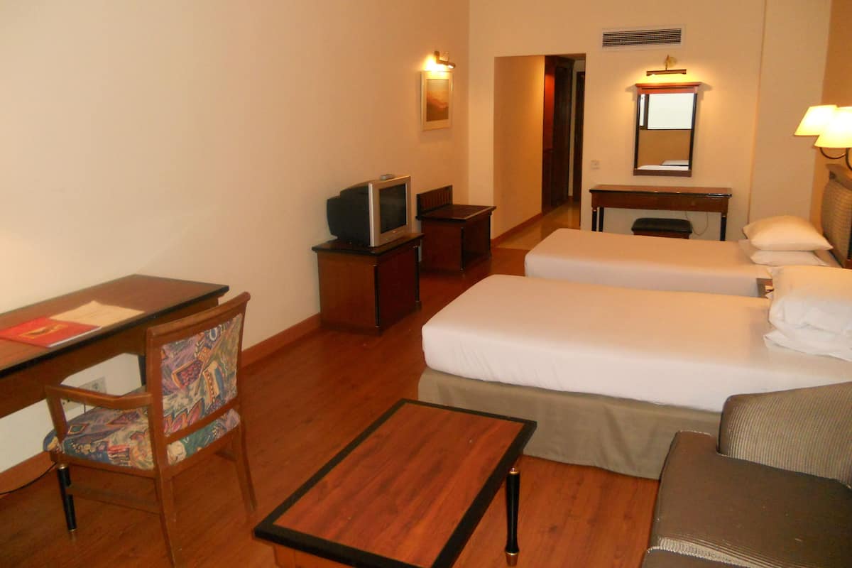 A hotel room with two beds, a desk, a chair, a television, and a small table.