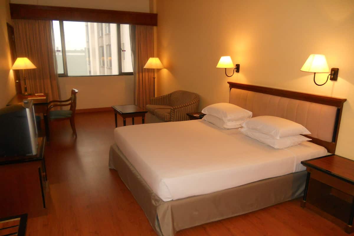 A hotel room with a large bed, two bedside lamps, a chair, a small table, and a window with curtains.