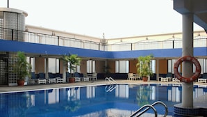 Une piscine entourée de chaises longues et agrémentée de plantes en pot, le tout surplombé d’un balcon doté de balustrades.