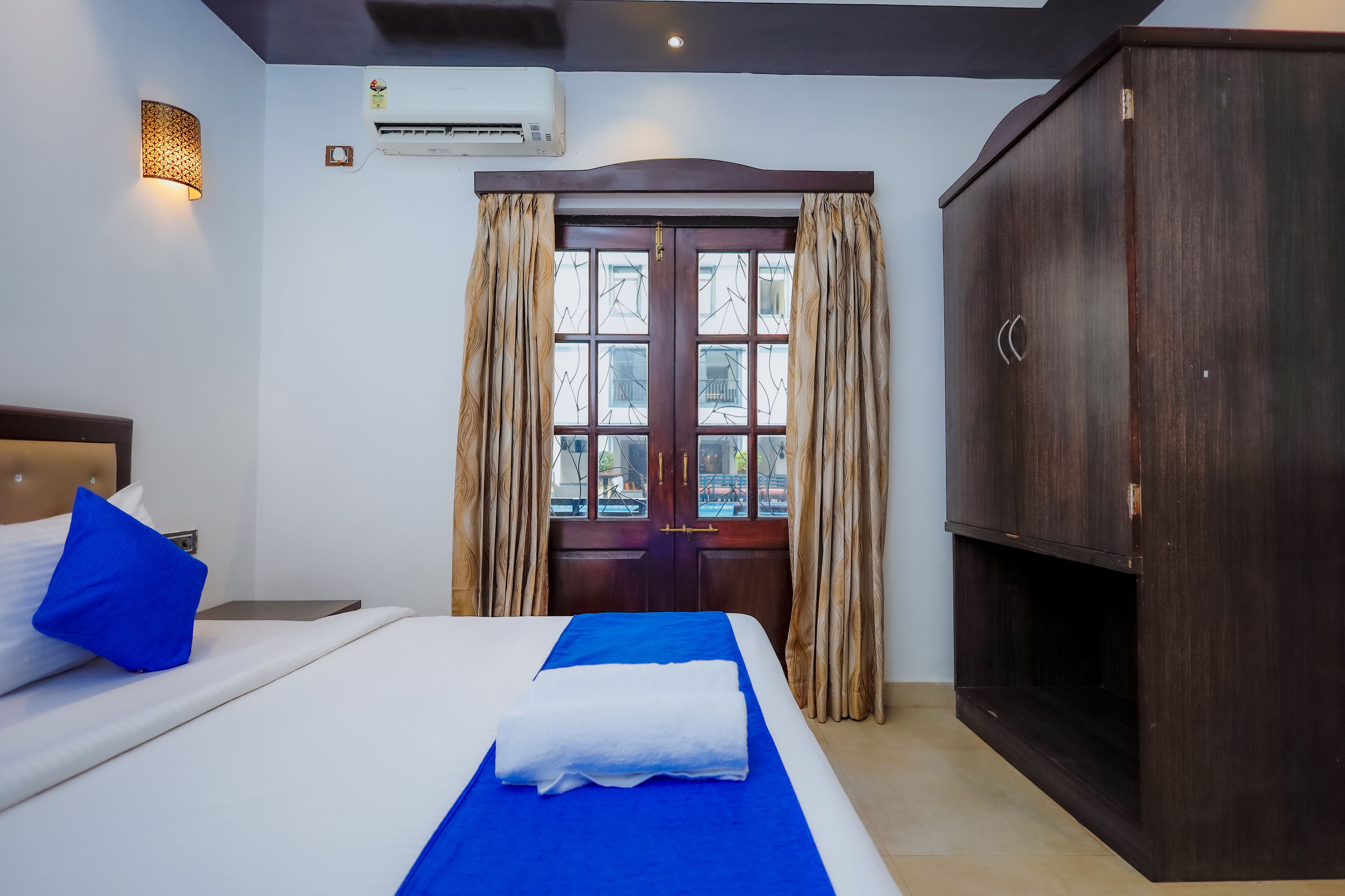 A hotel room with a bed, a wardrobe, and a window with curtains.