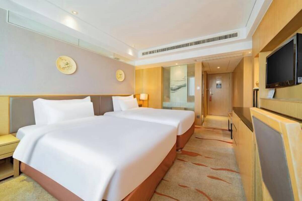 Ein Hotelzimmer mit zwei Betten, einem Fernseher, einer Uhr und einem Flur, der in ein weiteres Zimmer führt.