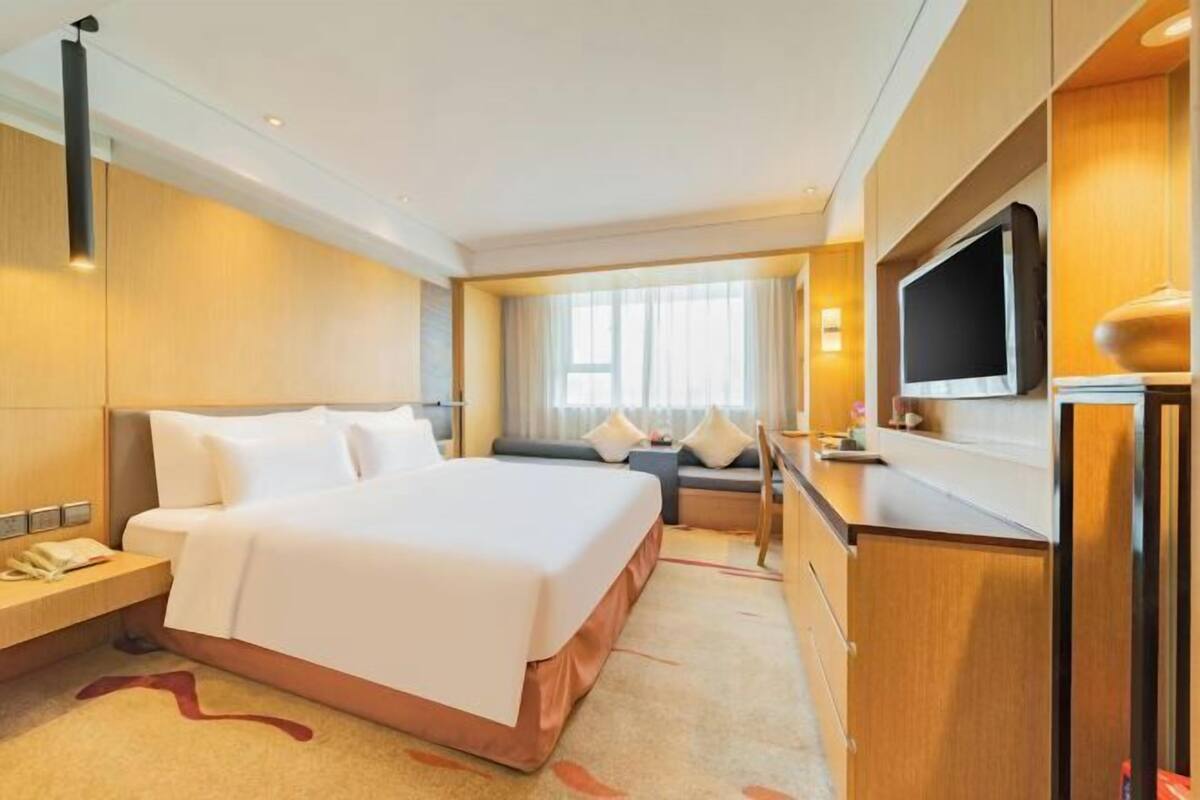 Ein Hotelzimmer mit einem großen Bett, einer Sitzecke, einem Schreibtisch mit Flachbildfernseher und einem Telefon.