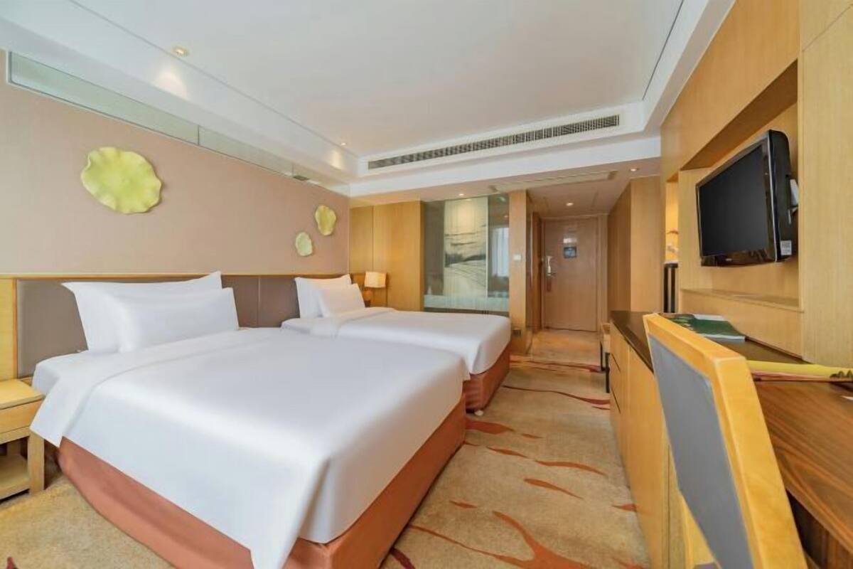 Ein Hotelzimmer mit zwei Betten, einem Schreibtisch mit Fernseher und einem durch eine Glastür einsehbaren Badezimmer.