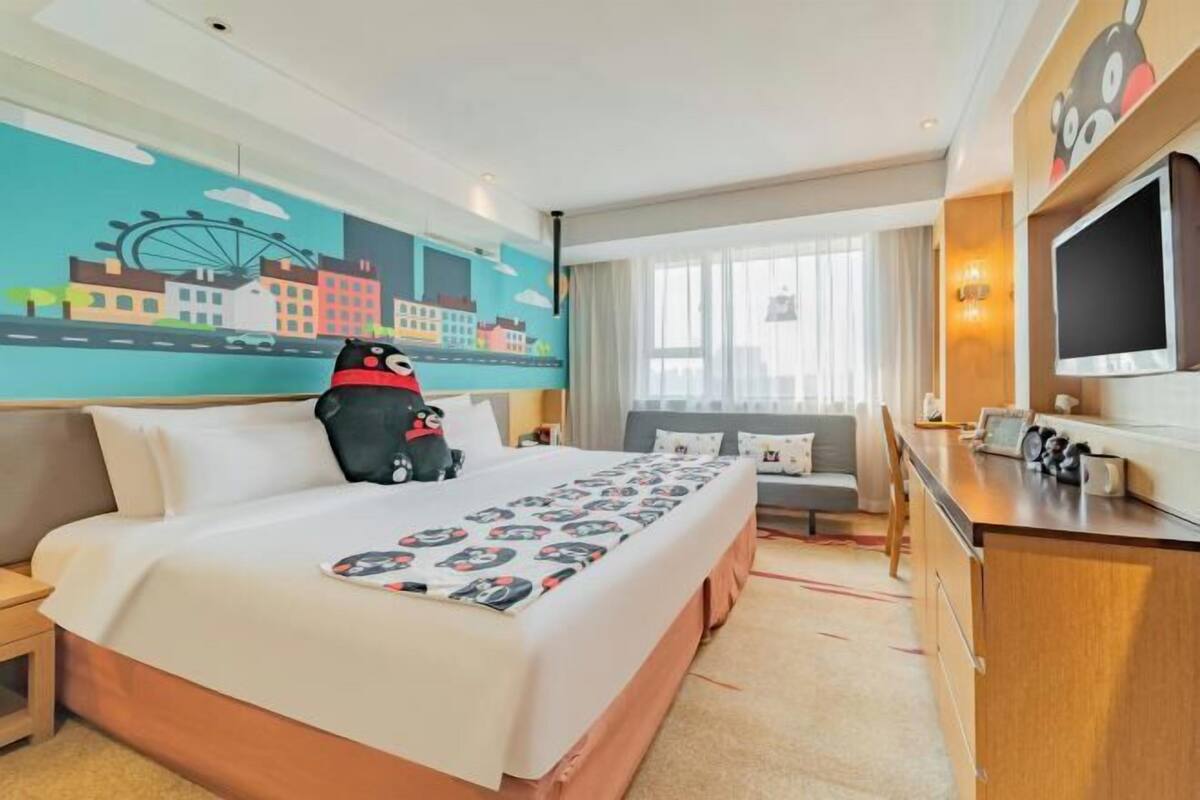 Ein Hotelzimmer mit einem Bett, einem Schreibtisch, einem Sessel, einem Fernseher und einem Wandgemälde.