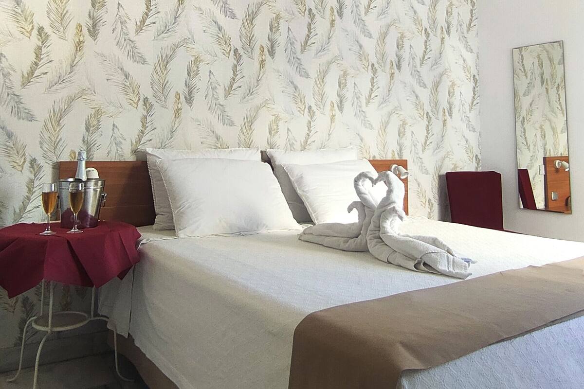 A hotel room with a bed, a bedside table with a red cloth, a wooden headboard, and a wall-mounted mirror.