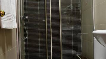 Un baño con ducha separada por mampara de vidrio, inodoro blanco y una toalla colgada en la pared.