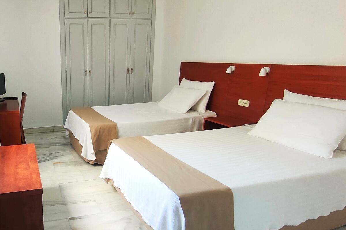 Two single beds with wooden headboards, a wardrobe, and a desk with a chair in a hotel room.