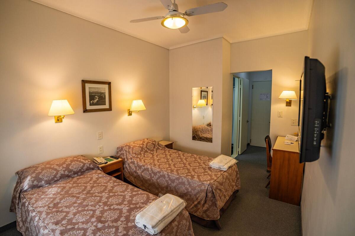 A hotel room with two beds, a ceiling fan, bedside lamps, a desk with a telephone, a mirror, and a television.