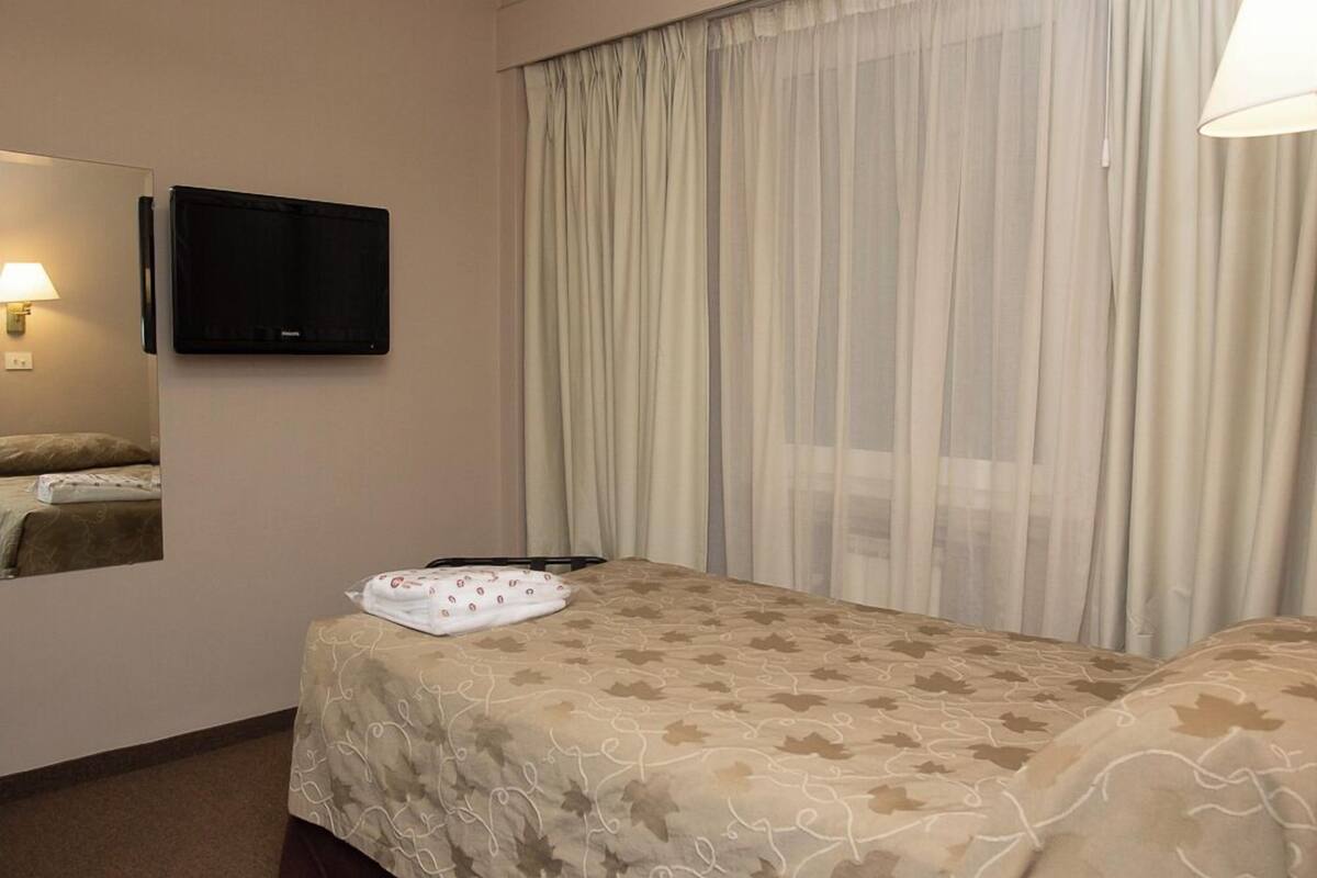 A hotel room with a bed, a television mounted on the wall, and a window with curtains.