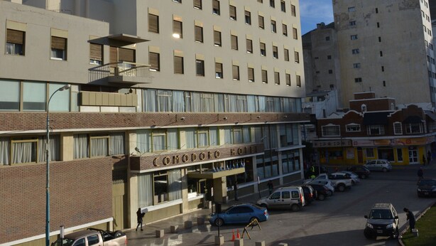 A hotel with a modern facade, multiple floors, and a parking area with several cars.