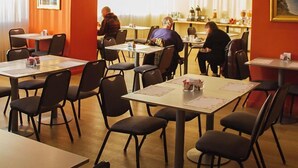 A dining area with tables and chairs, a counter with a menu, and a view of the sea through large windows.