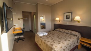 A hotel room with a bed, a desk, a chair, a ceiling fan, and two wall-mounted lamps. - Comodoro Hotel (Comodoro Rivadavia)