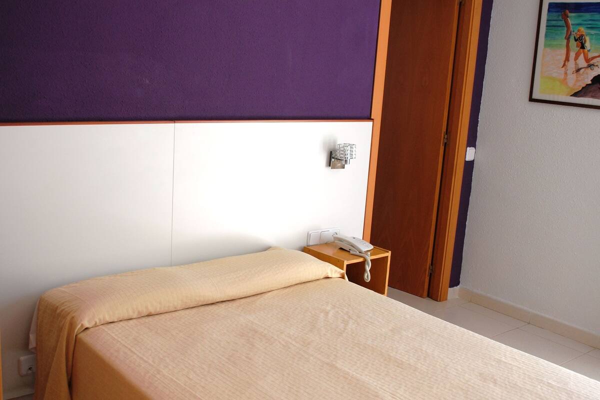 A hotel room with a bed, a bedside table with a phone, and a door.