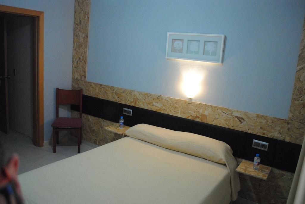 Una habitación de hotel con una cama, una silla y una lámpara fijada a la pared.