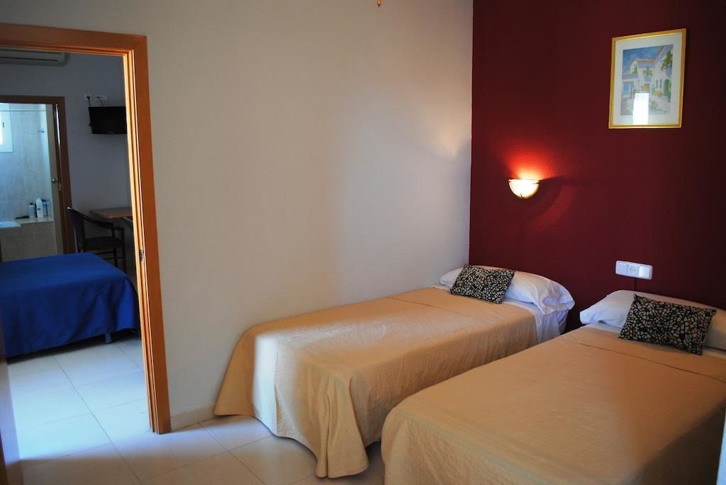 A hotel room with two single beds, a red accent wall, a framed picture, and a bedside lamp.