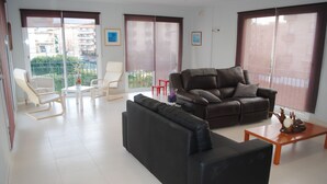 Una sala de estar con un sofá negro, un sillón blanco y una mesa de centro de madera.