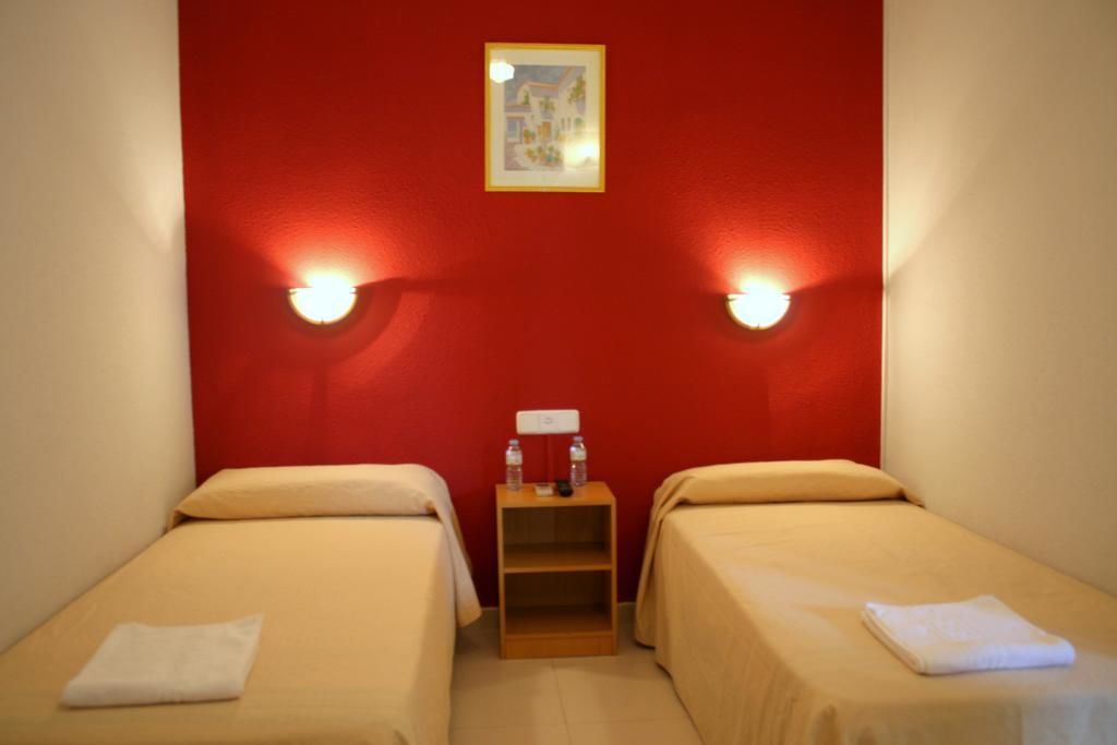 A room with two single beds, a small wooden nightstand with a lamp, and a framed picture on the wall.