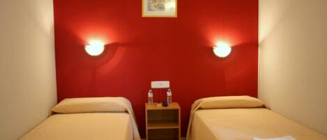 A room with two single beds, a small wooden nightstand with a lamp, and a framed picture on the wall.