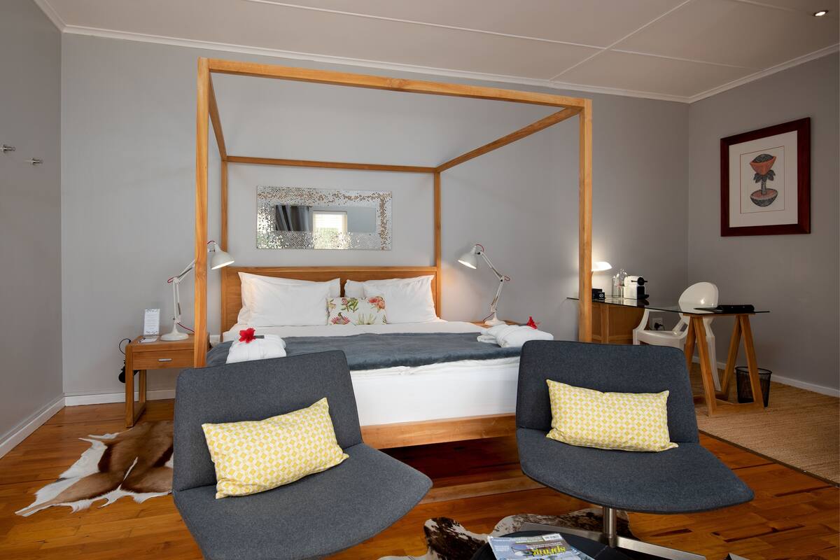 A bedroom with a four-poster bed, two armchairs, a desk, and a mirror.
