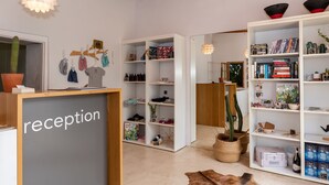 Zona de recepción con mostrador, estanterías con libros y objetos decorativos, un cactus y una alfombra de cuero.