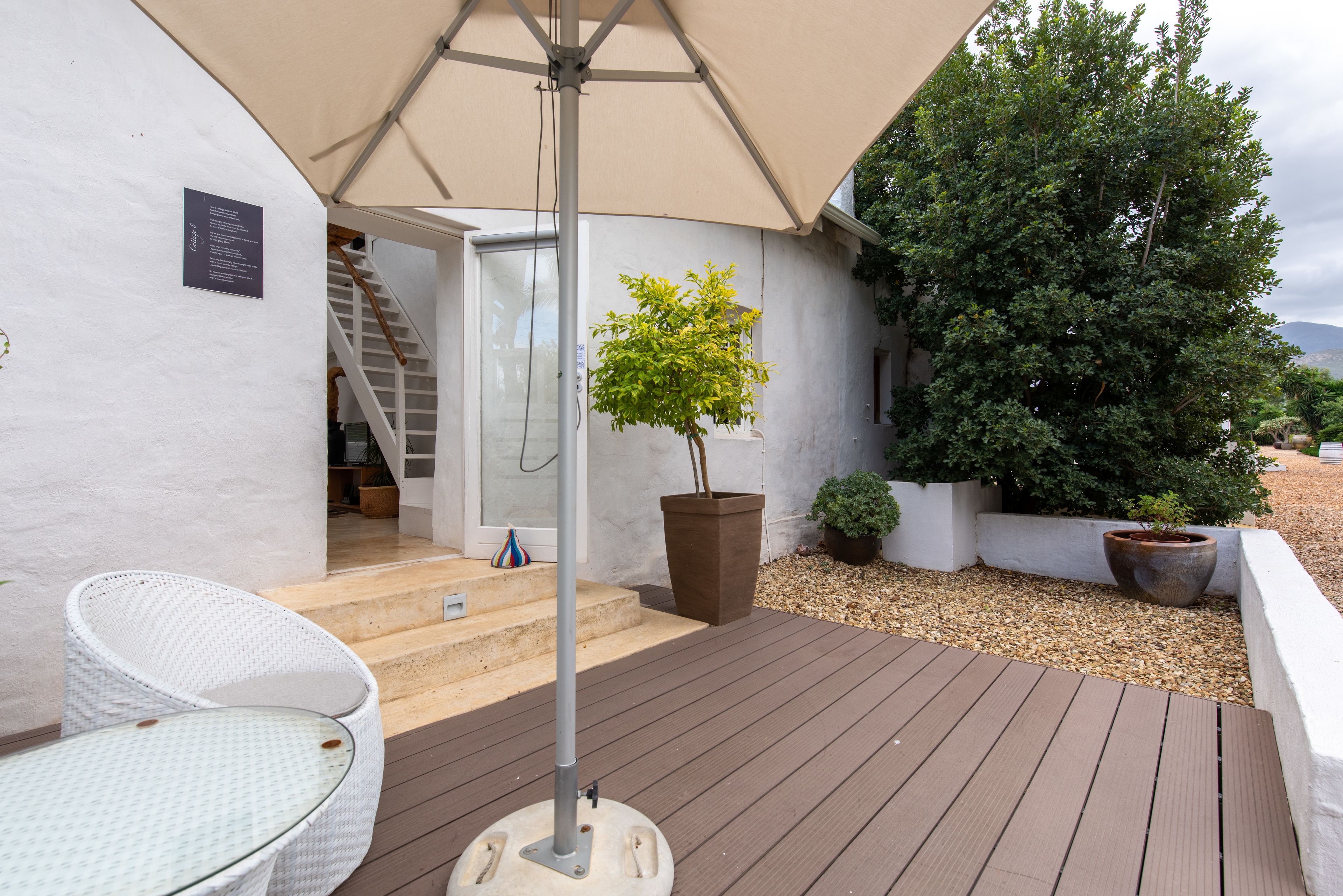 Une terrasse en bois avec une chaise en osier blanche, une plante en pot et un grand parasol.