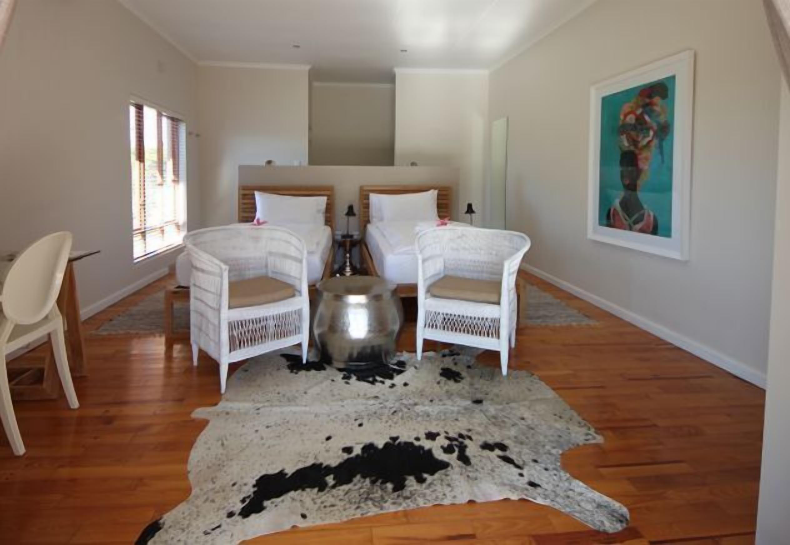 A room with two white wicker chairs, a large cowhide rug, and a bed with wooden headboards.