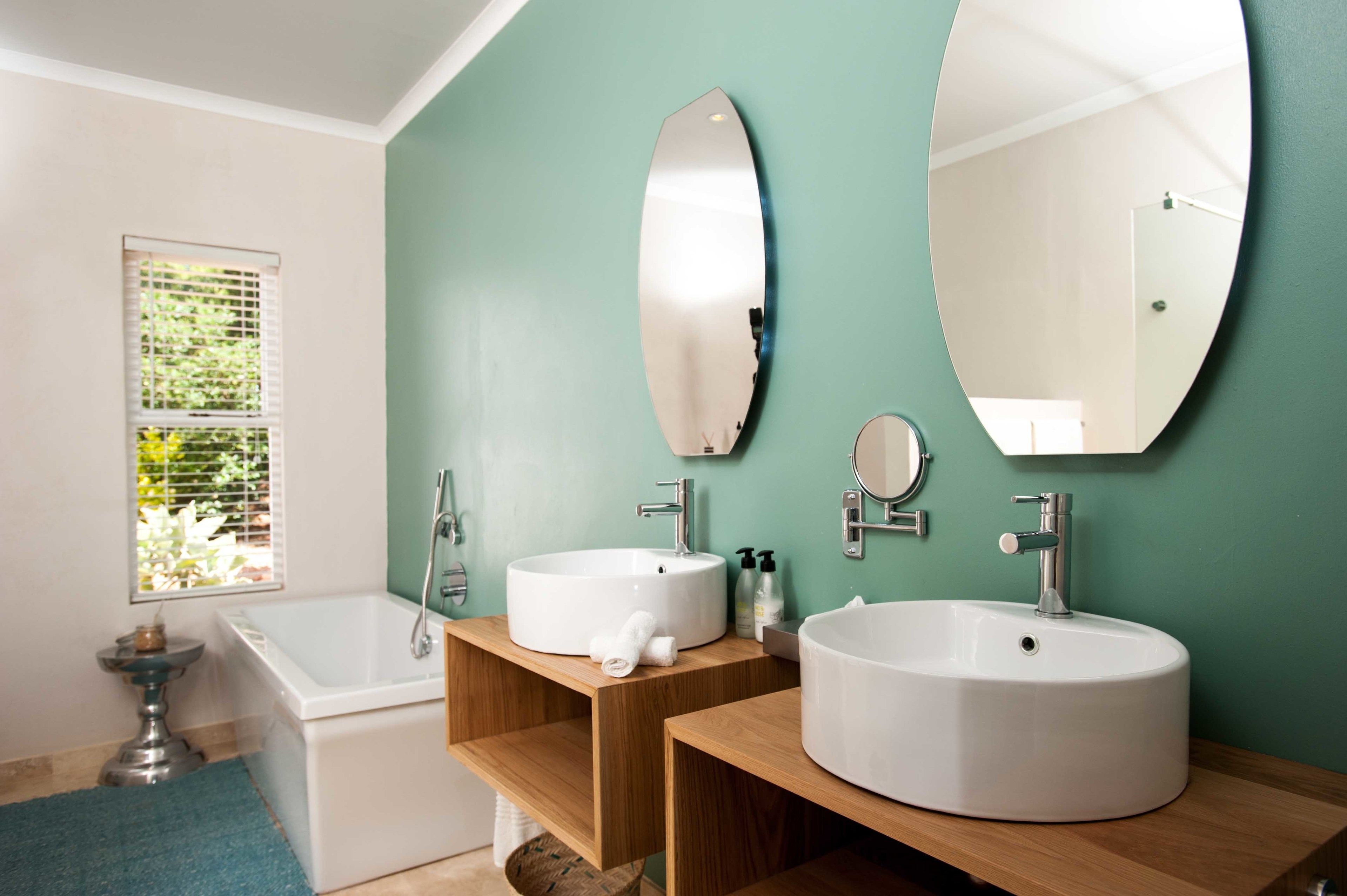 A bathroom with two sinks, a bathtub, and a window with blinds.