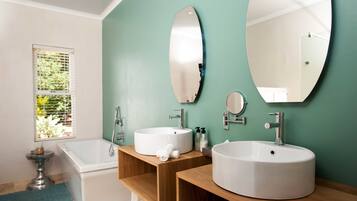 A bathroom with two sinks, a bathtub, and a window with blinds.