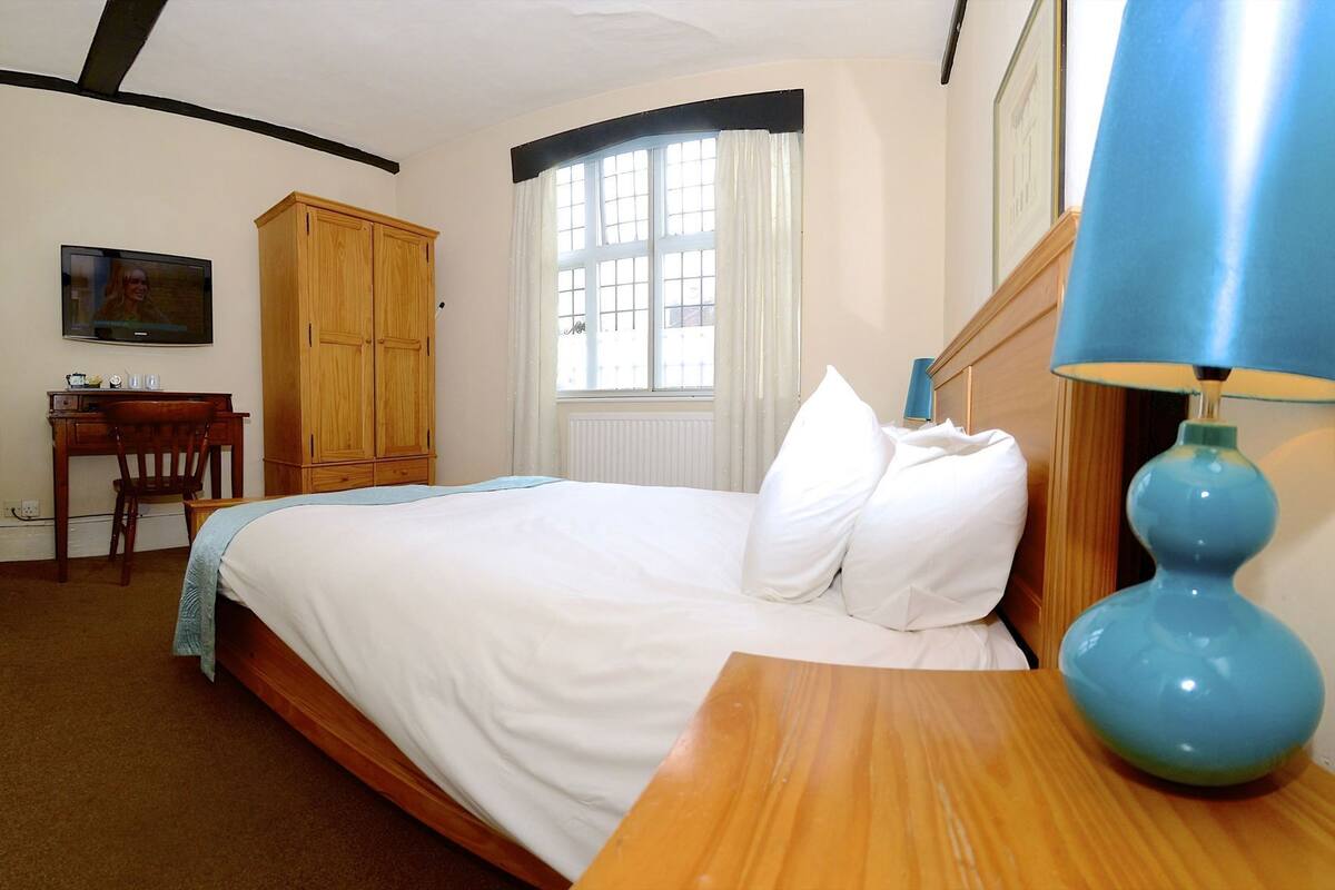 Une chambre à coucher comprenant un lit, un bureau, une chaise, une armoire et une fenêtre avec des rideaux.