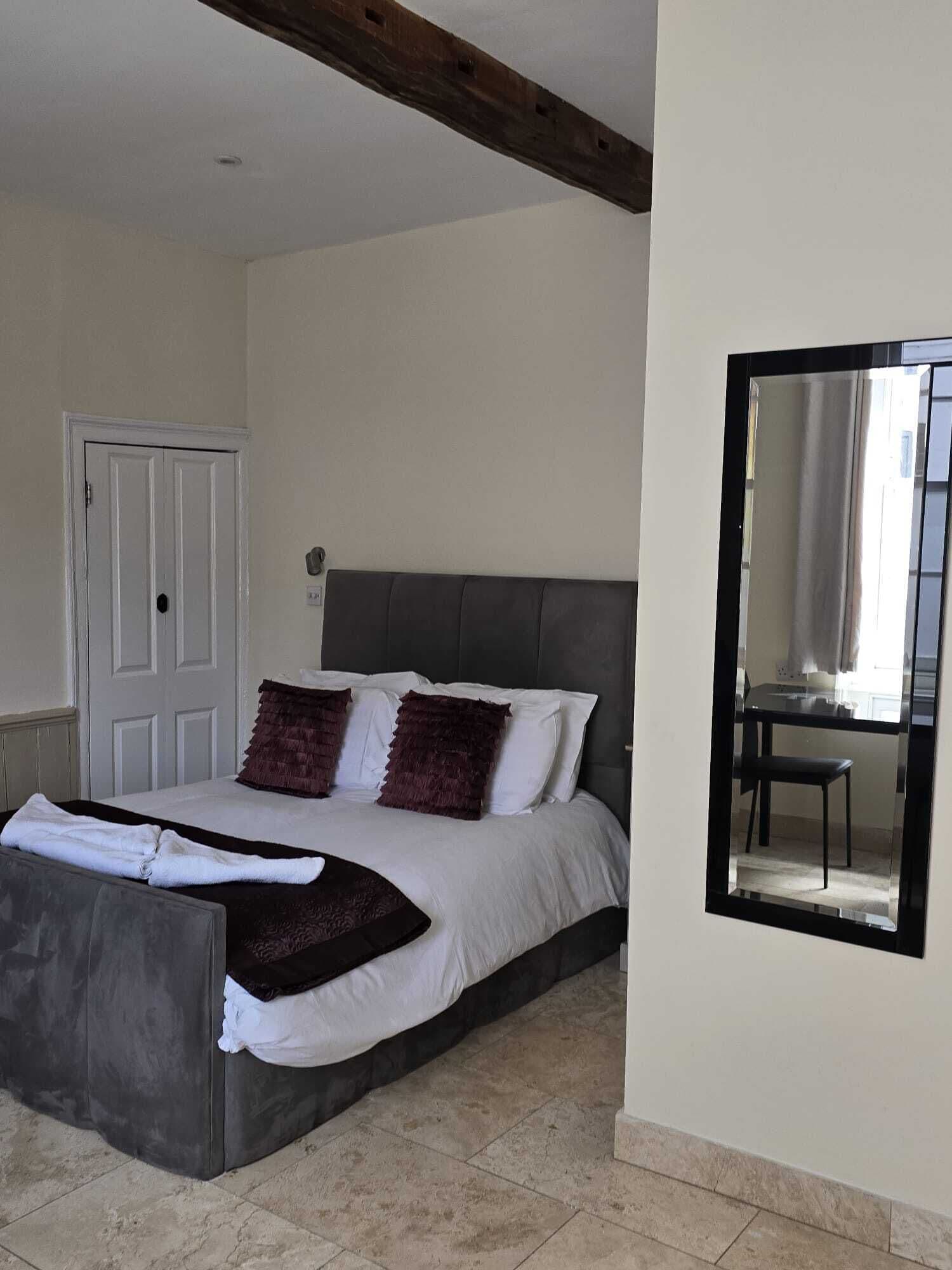 A bedroom with a bed, a chair, a door, and a mirror on the wall.